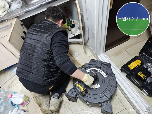 싱크대 하부장을 열고 스프링 장비로 배수관을 뚫는 모습